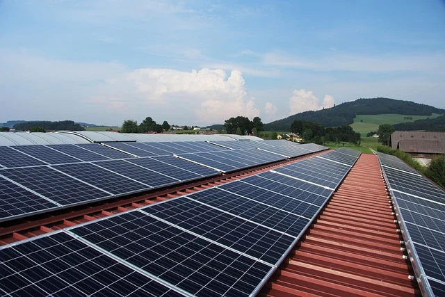 Solar panels on a large red roof with a rural landscape background.