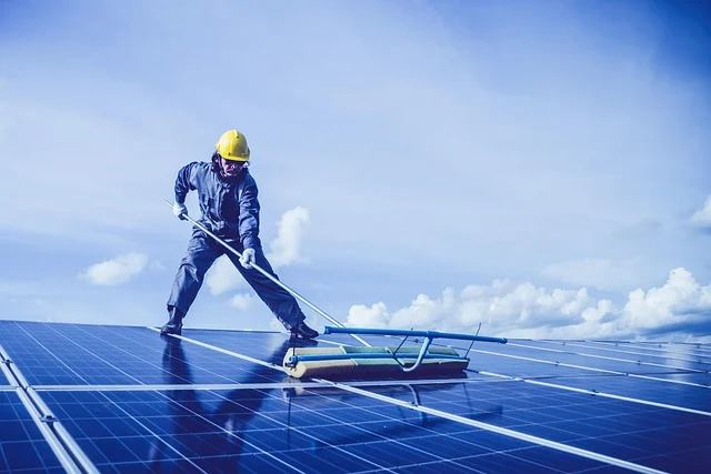 Worker cleaning solar panels under a blue sky.