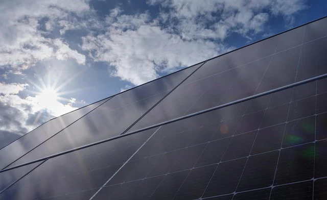 Solar panels with the sun shining and clouds in the sky.