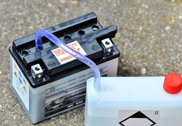 A lead-acid battery being filled with electrolyte from a plastic bottle.