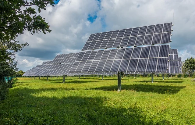Rows of solar panels in a field under a partly cloudy sky.