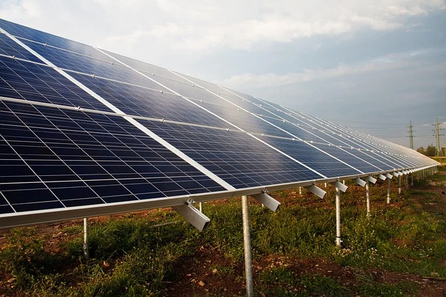 A large array of ground-mounted solar panels under a cloudy sky.