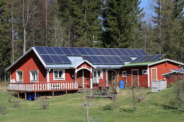 A red house with solar panels on the roof, surrounded by trees.